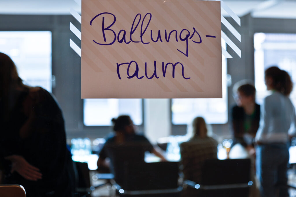 Raumschild "Ballungsraum" beim Barcamp, dahinter undeutlich Menschen