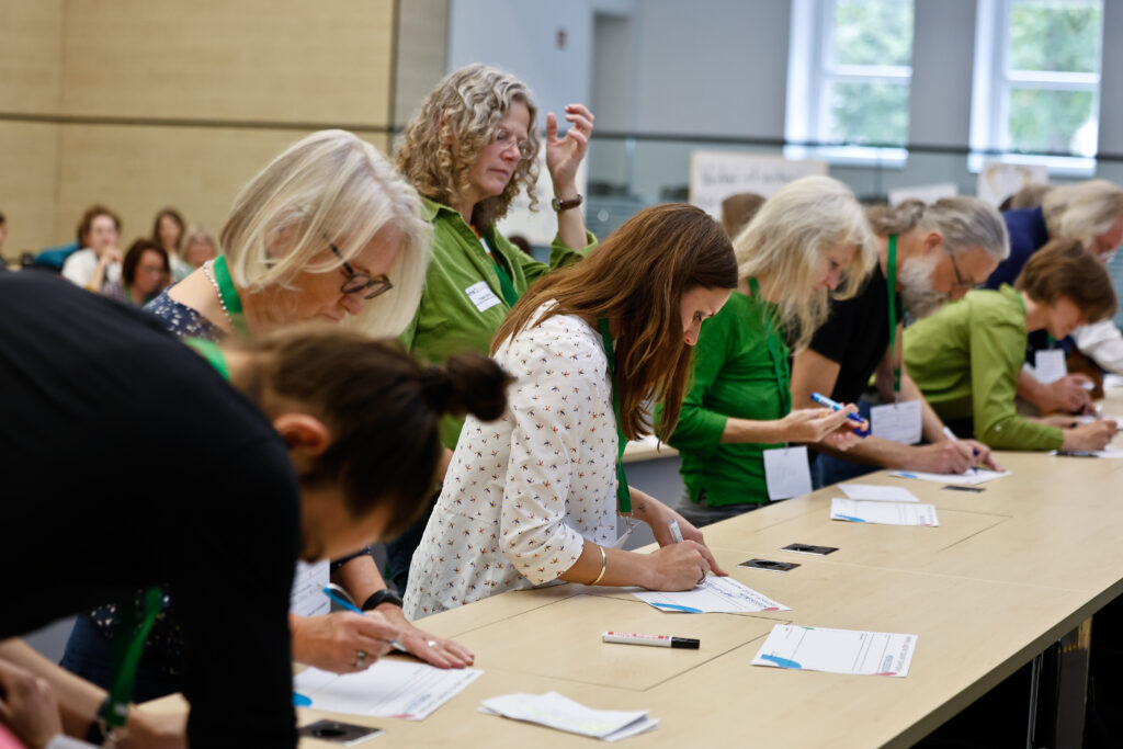 unterschiedliche Menschen schreiben an Tischen ihre Vorschläge für Barcamp-Sessions