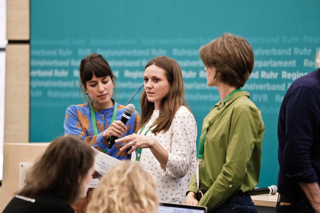 3 Frauen, eine am Mikrofon erklärt ihren Vorschlag